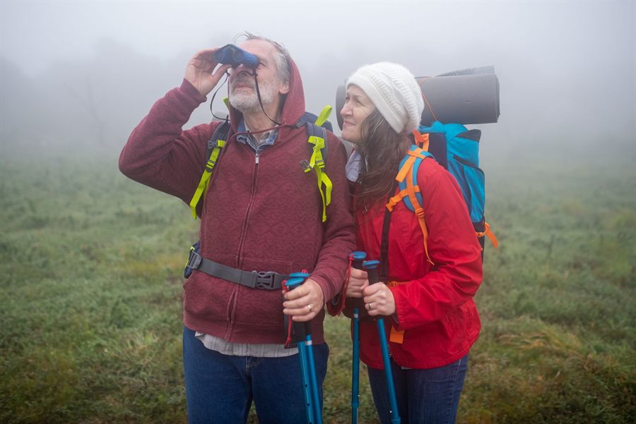 Two travelers in rain jackets looking through binoculars