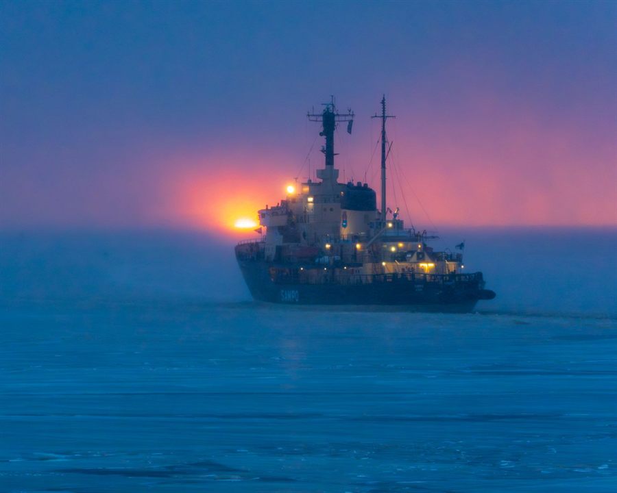 Expedition cruise ship silhouetted at sea under a red sunset