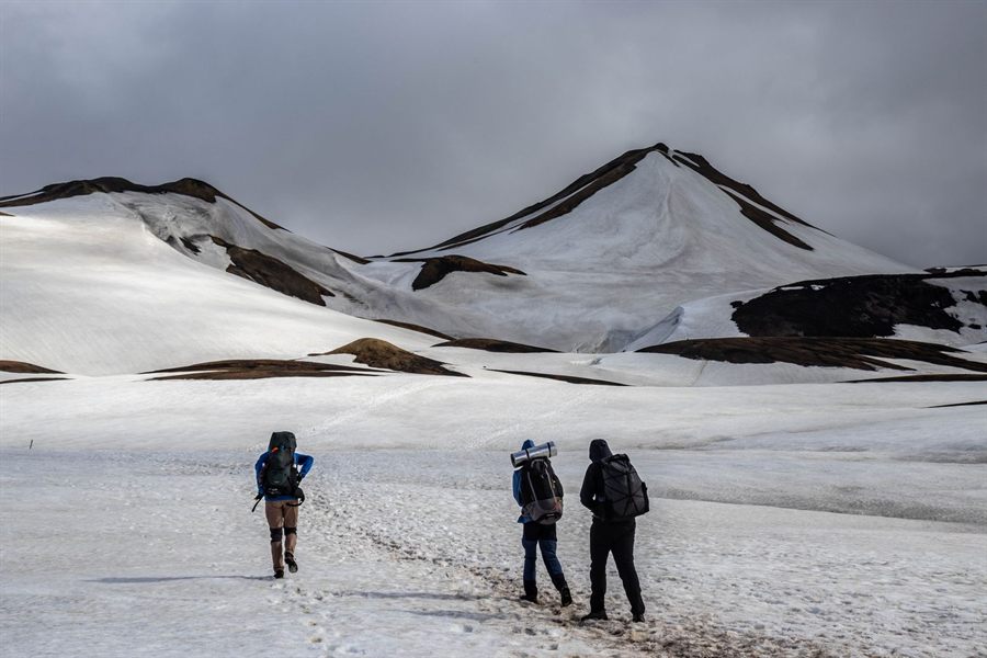 Hikers crossing a snowfield below dark volcanic peaks