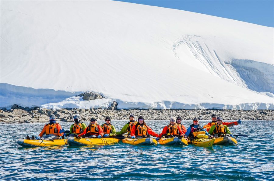 Group of kayakers paddling past a snowy glacier shore