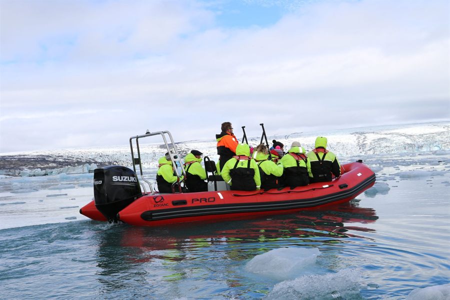 Group in life jackets riding a red inflatable boat through icy water